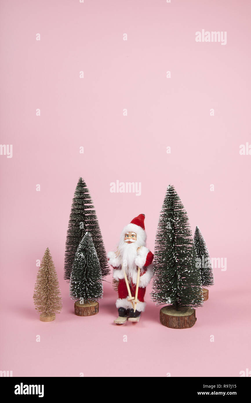 Ein Weihnachtsmann Figur Skifahren unter Miniatur Tannen auf einem rosa Hintergrund. Farbharmonie. Minimale noch leben Farbe Fotografie Stockfoto