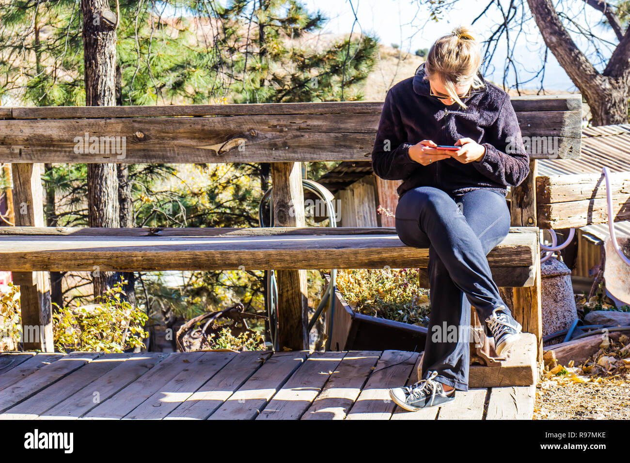 Frau SMS auf Handy beim Sitzen auf rustic Bank Stockfoto