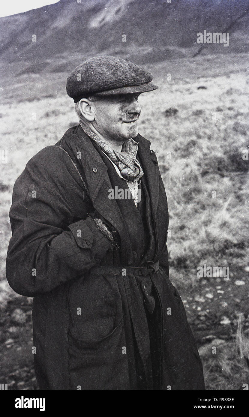 1940, historische, eine walisische Kohle Miner in Mantel und flatcap zu Fuß von einem Hügel, in einem Tal bei Merthyr, South Wales, UK. Stockfoto