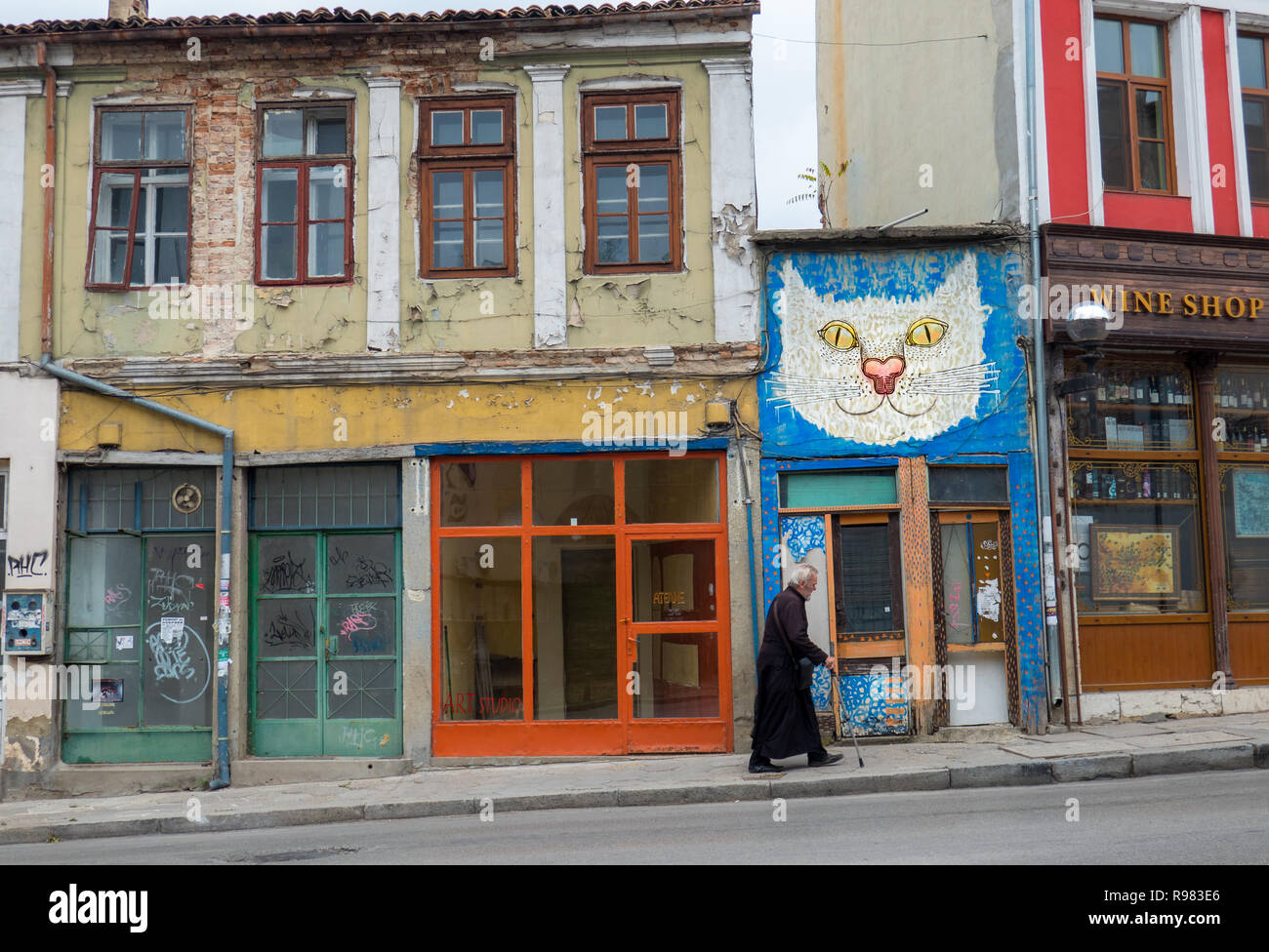 Typische Straße von Veliko Tarnovo, wo viele Geschäfte heute mit Katzenkunst geschlossen sind. Ein alter Mann trägt Schwarz und einen Stock, der den Hügel hinaufgeht Stockfoto