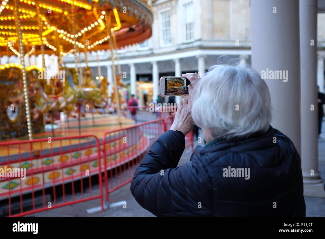 Reife Frau verwendet Smart Phone zu fotografieren Messegelände fahren. Weihnachtsmarkt in Bath, UK. Stockfoto