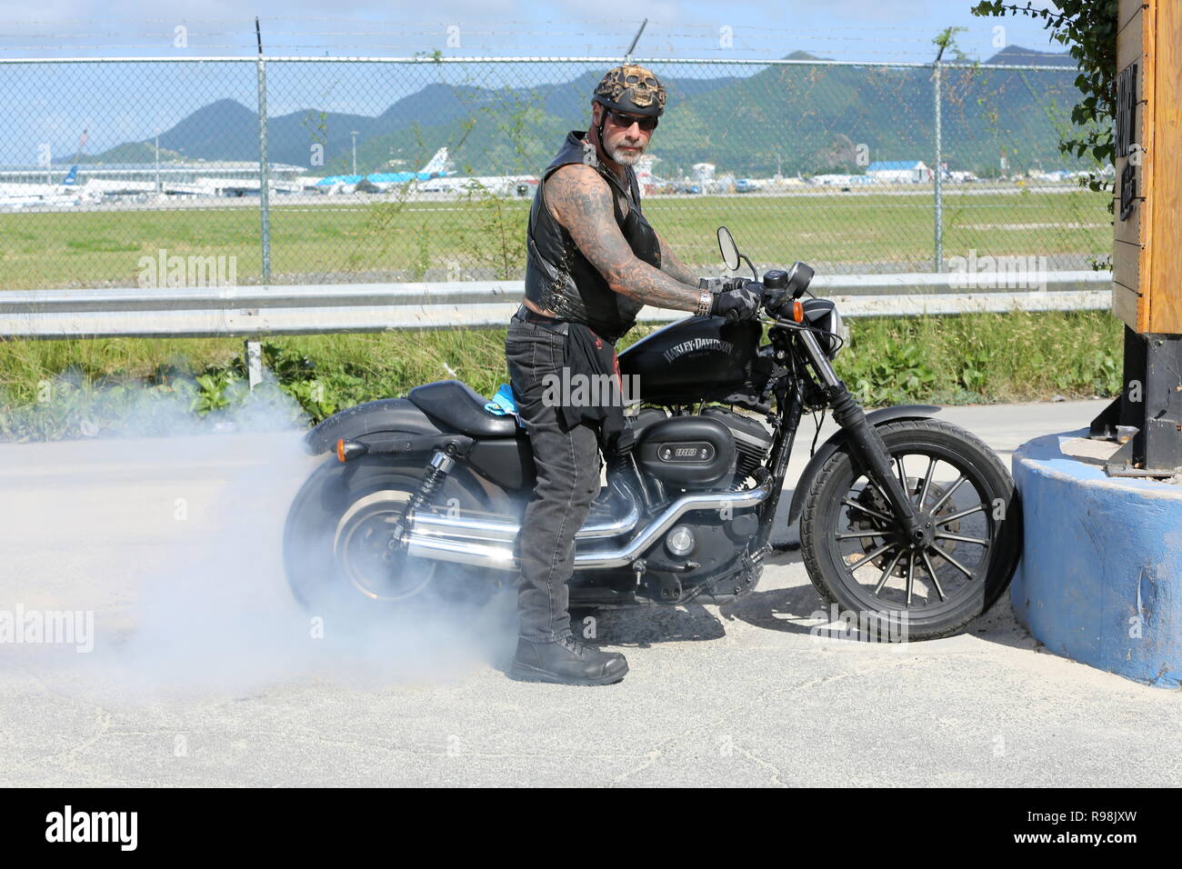 Ein Hells Angel auf seiner Harley Davidson 833 Sportster gelegt, ein wenig Brennen Gummi Demonstration für die Kamera in der Nähe des Sunset Beach Bar auf Sint Maarten Stockfoto