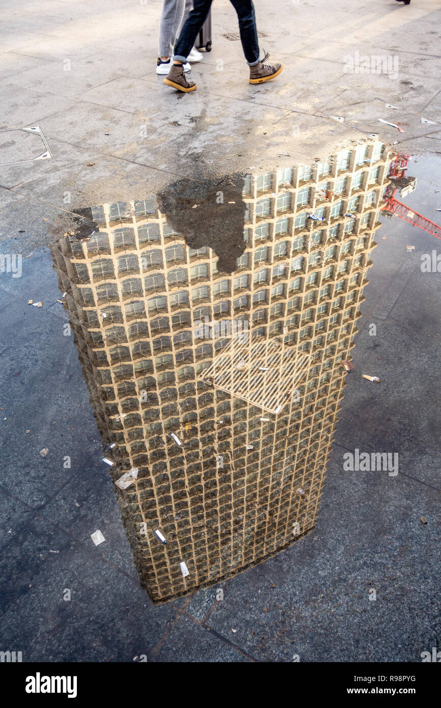 Reflexion von Menschen zu Fuß in der Nähe von einem regen Pfütze und kopfüber Mittelpunkt eines 33-stöckigen Büroturm Block in der Nähe der Tottenham Court Road und die Oxford Street Stockfoto
