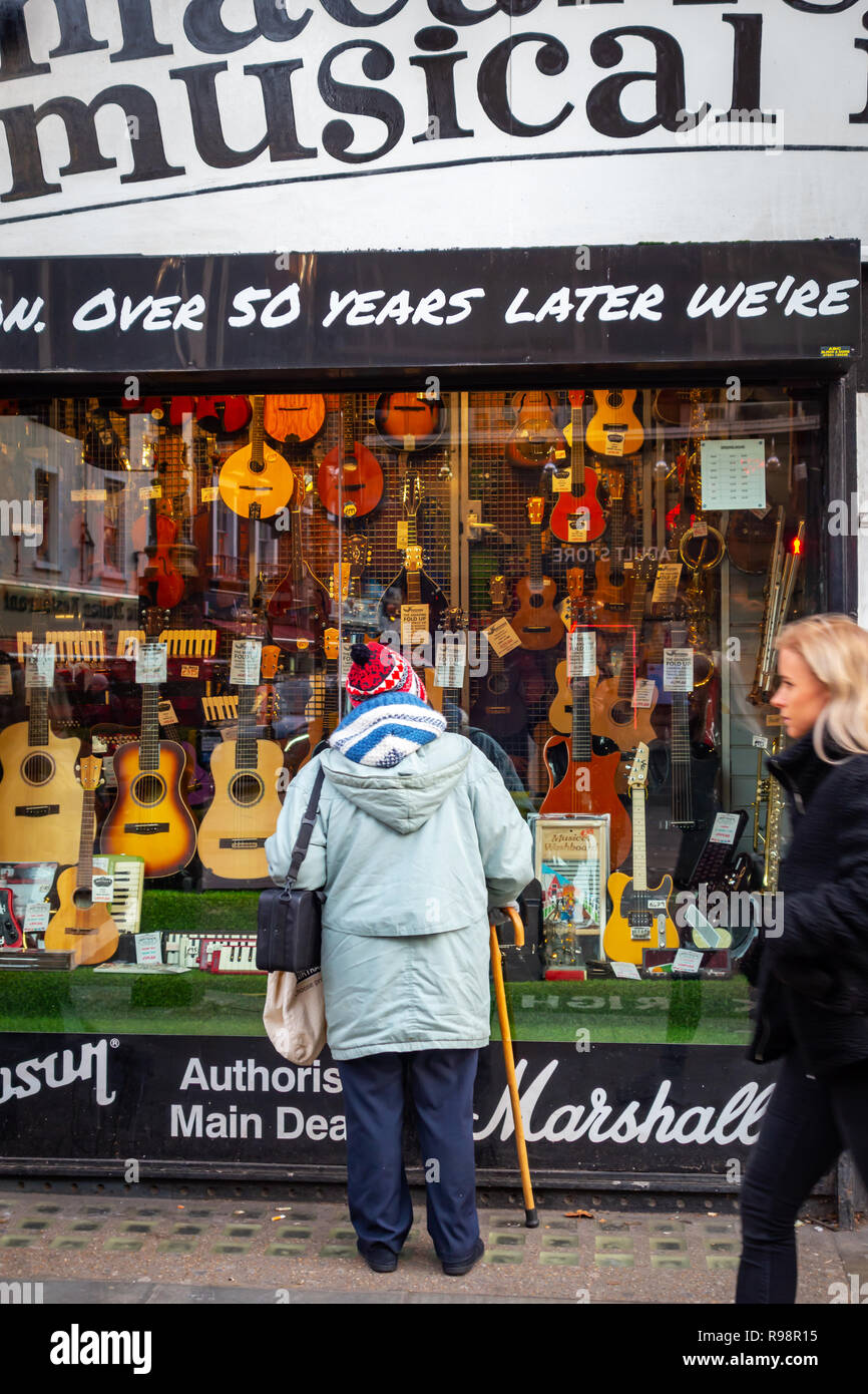 Ältere Dame in den Store Shop vor der berühmten macaris Musikinstrumente shop in Charing Cross Road, London suchen Stockfoto