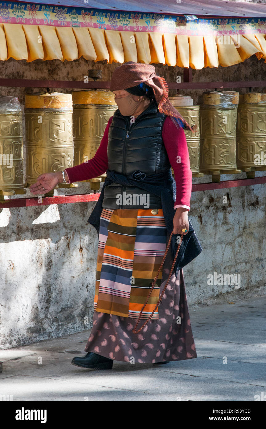 Eine weibliche Pilger dreht Gebetsmühlen entlang der Kora oder Pilgerreise Pfad unterhalb des Potala Palace in Lhasa, Tibet, China Stockfoto