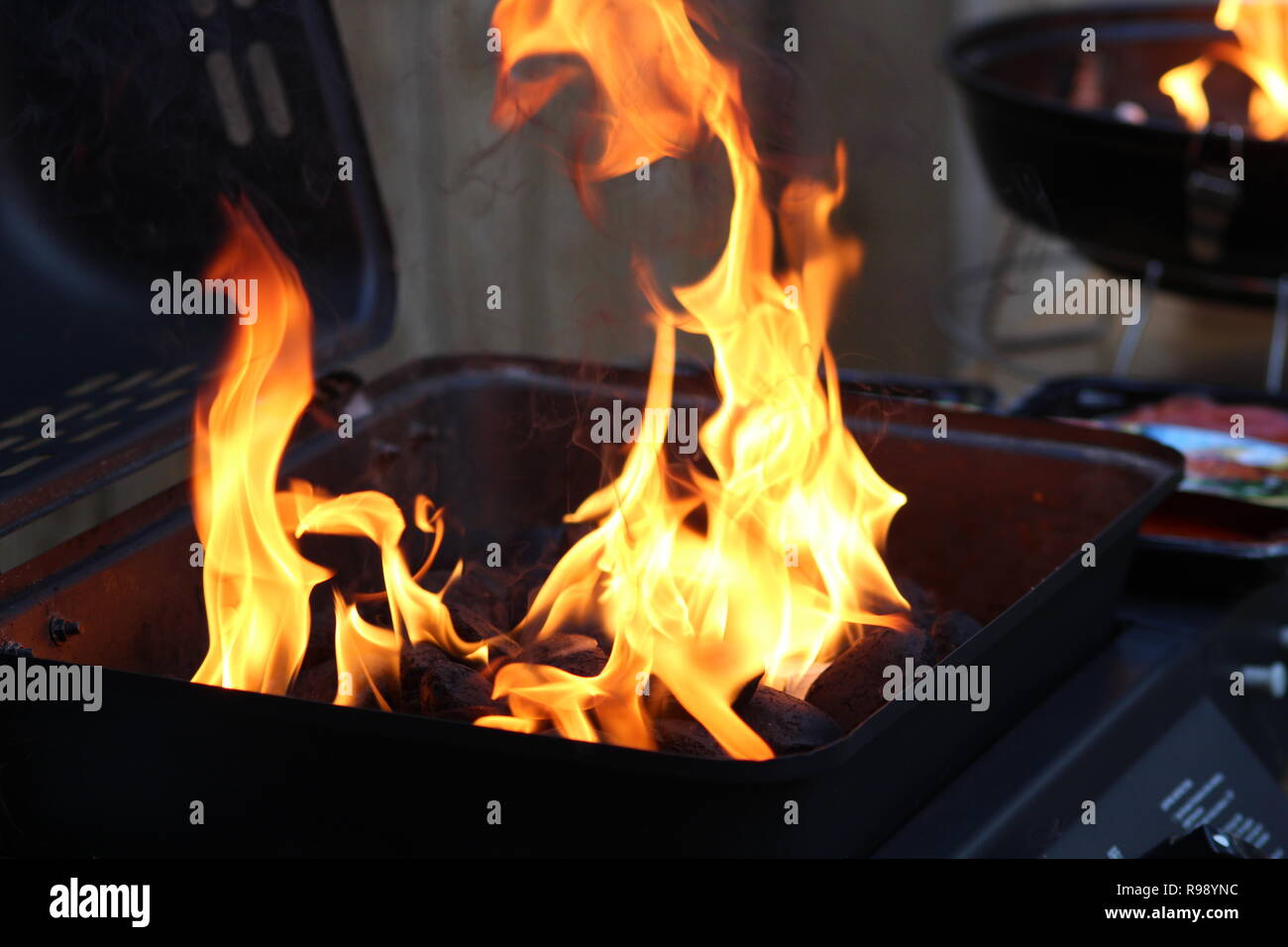 Große Flammen steigen von einem Grill gerade im Sommer beleuchtet Stockfoto