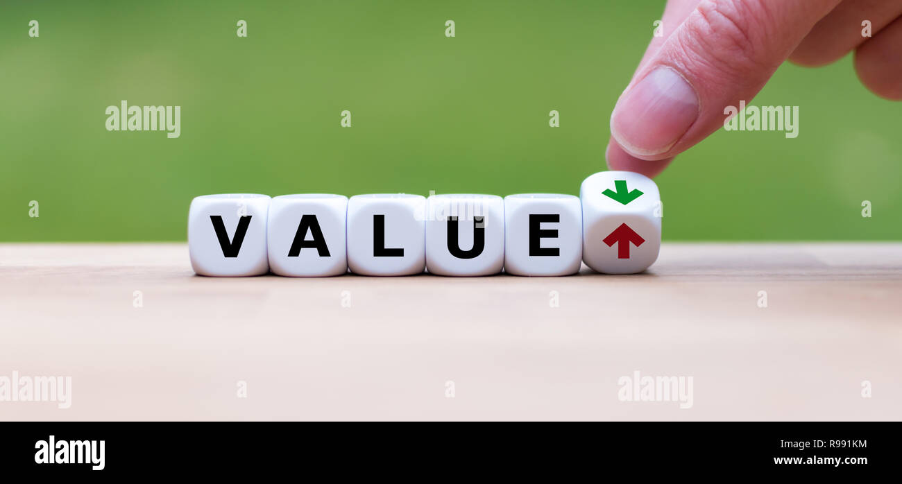 Hand dreht einen Würfel und verändert die Richtung, in die sich ein Pfeil symbolisiert, dass der Wert von etwas wird (oder umgekehrt) Stockfoto