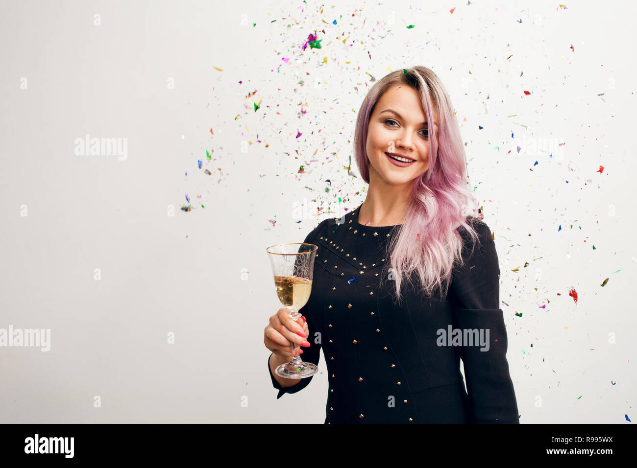 Lustige junge Frau in schwarzem Kleid zu feiern. Schöne junge Frau mit einem Glas Champagner und Konfetti Stockfoto