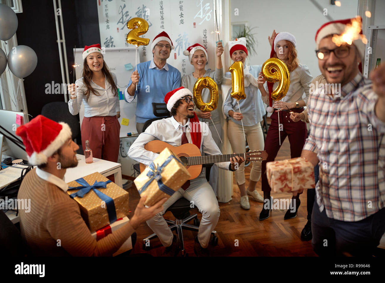 Lächelnd Business Team Spaß haben und tanzen in Santa Hut auf Xmas Party und zum Austausch der Geschenke im Büro Stockfoto