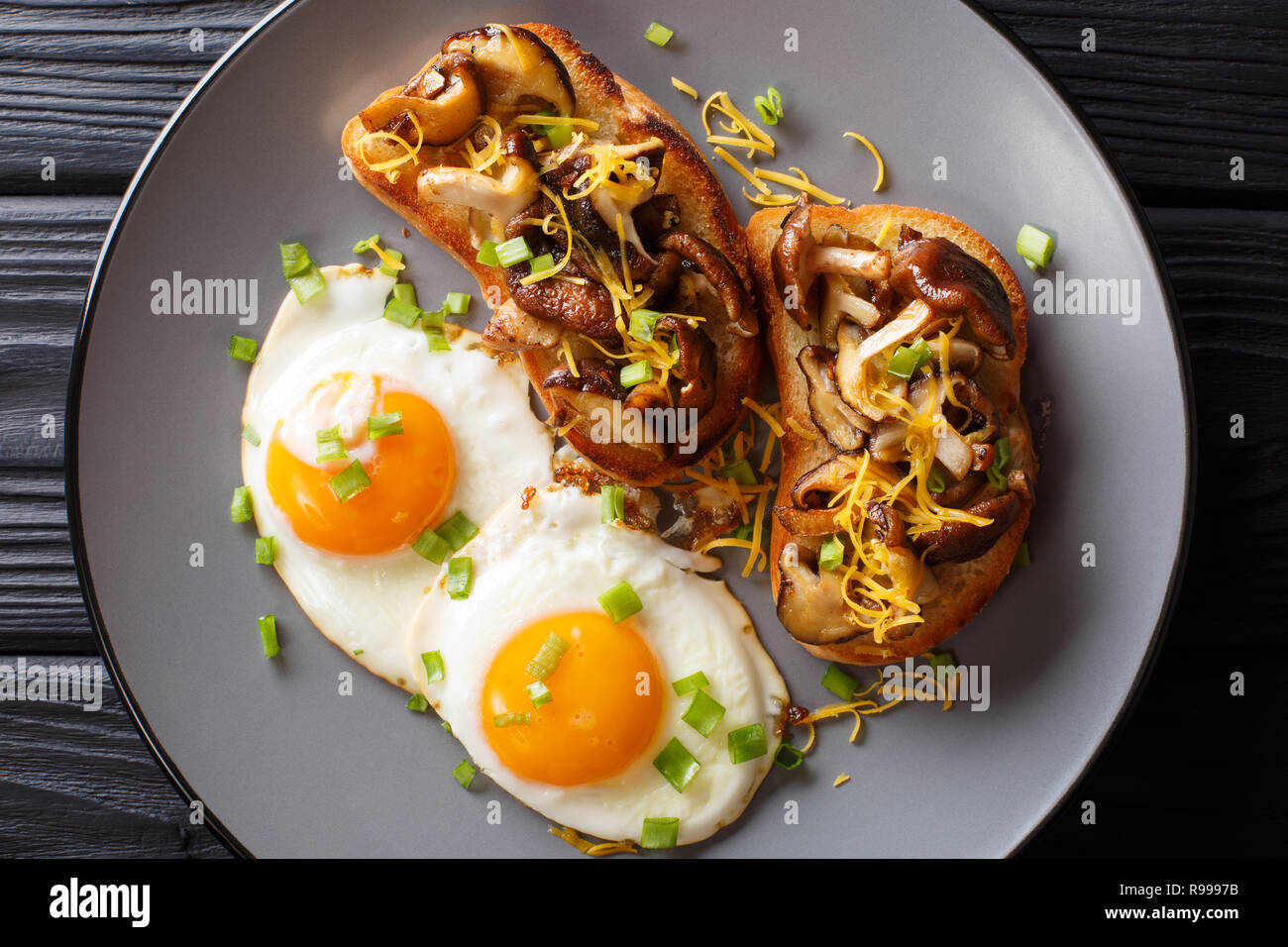 Leckeren Toast mit Shiitake Pilze und Cheddar Käse mit Spiegelei in der Nähe serviert auf einem Teller auf den Tisch. horizontal oben Ansicht von oben Stockfoto