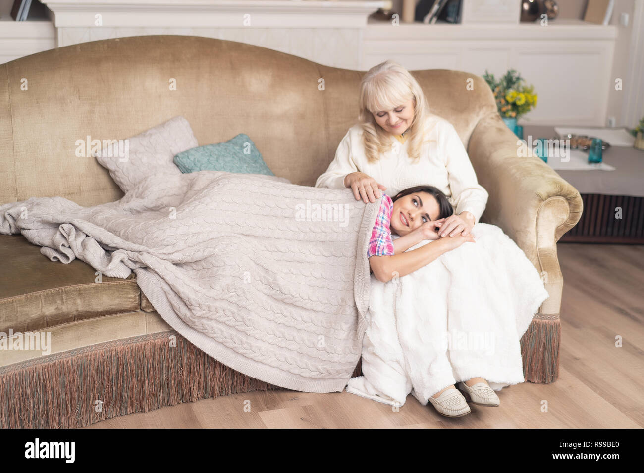 Allgemeine Schoß der Familie. Verschlafene Tochter liegt im warmen Decke auf Mutters Runden. Alte Frau sitzt auf dem Sofa, während ihre junge Tochter Stockfoto