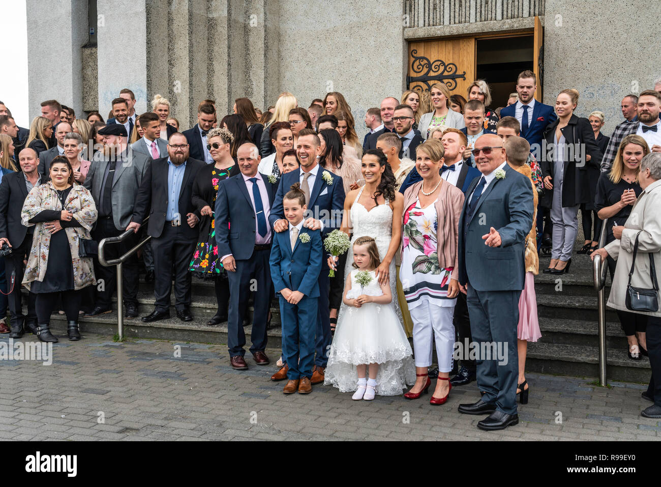 Hochzeit Gäste für ein Gruppenfoto vor dem Akureyrarkirkja, Evangelische Kirche in Akureyri, Island, Europa aufwirft. Stockfoto