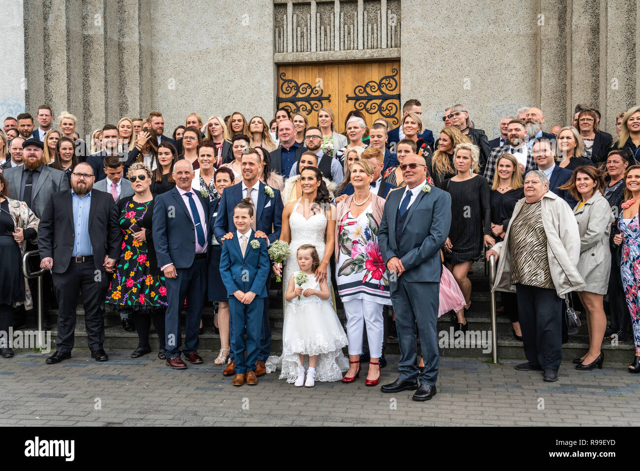 Hochzeit Gäste für ein Gruppenfoto vor dem Akureyrarkirkja, Evangelische Kirche in Akureyri, Island, Europa aufwirft. Stockfoto
