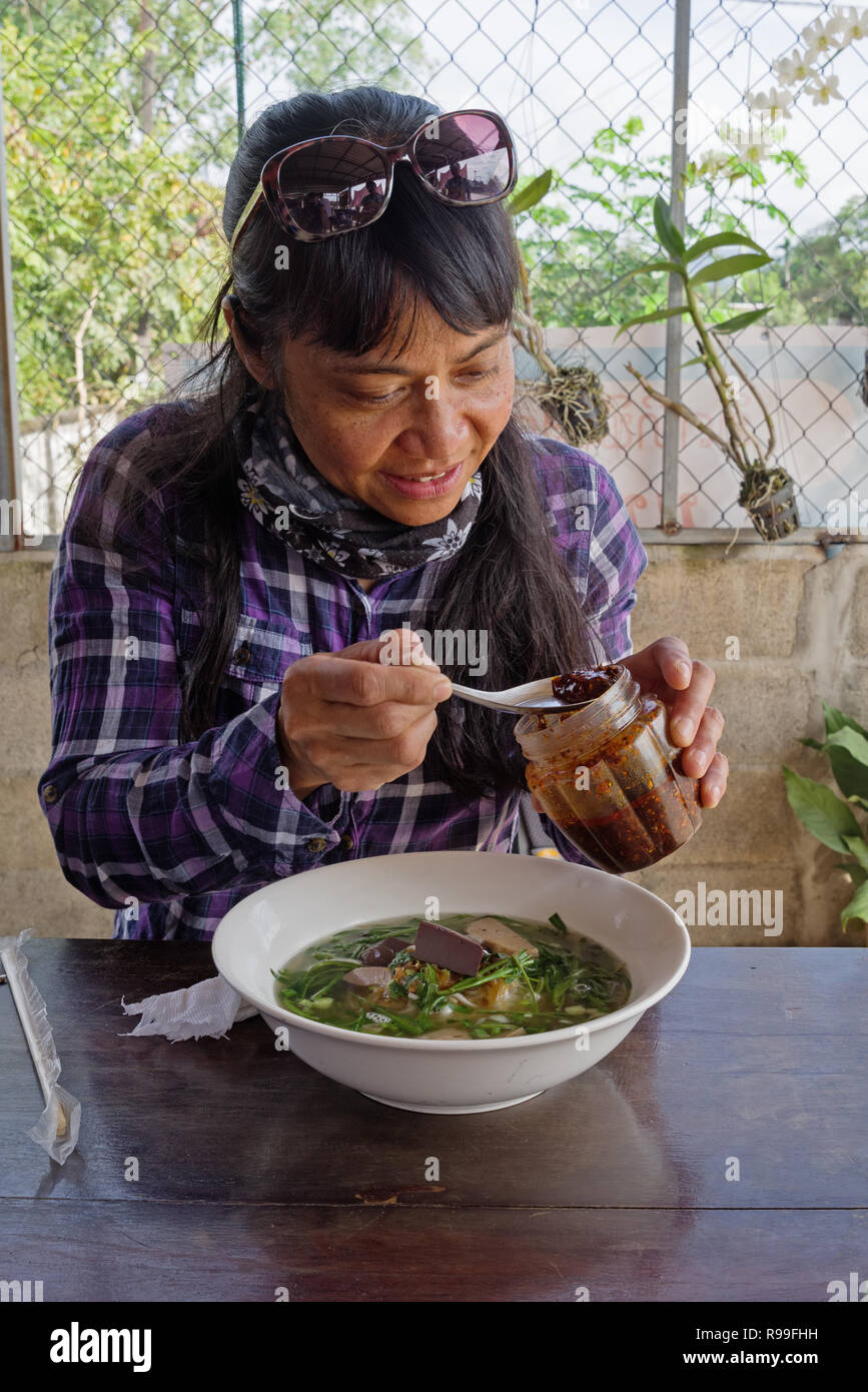 Frau setzen hot chili Öl in eine Schüssel Nudelsuppe in Laos. Stockfoto