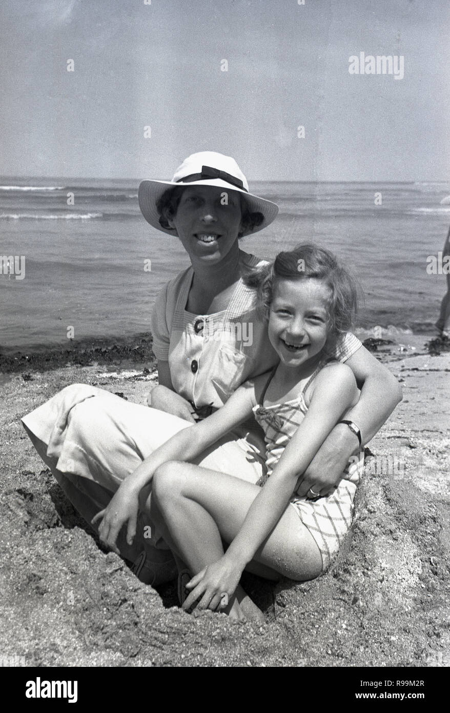 1940 s, historischen, Mutter mit ihr glücklich lächelnde Tochter sitzen zusammen an einem Strand. Stockfoto