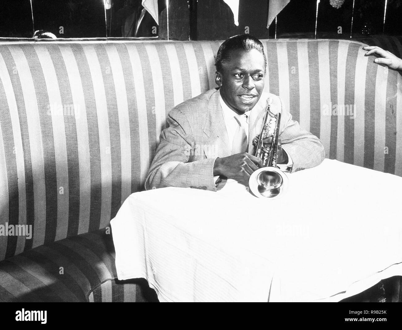 American Jazz musiker Miles Davis hält seine Trompete und lächelt, als er in einem gestreiften stand auf der Birdland Nachtclub sitzt, New York City, 1949. Stockfoto