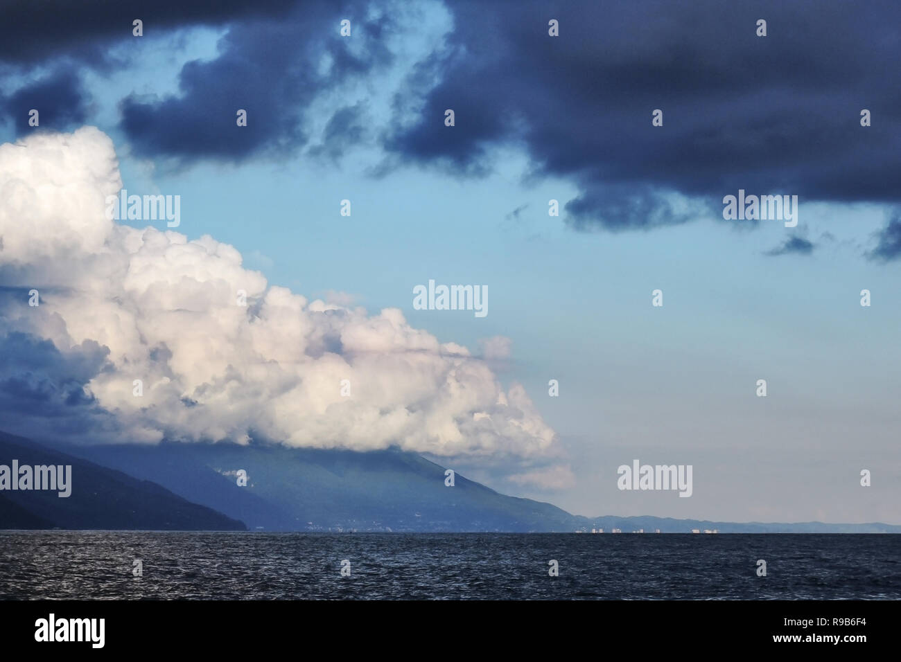 Pyrocumulative und Gewitterwolken, die teilweise von der Sonne beleuchtet, über die Berge und das Meer. Stockfoto