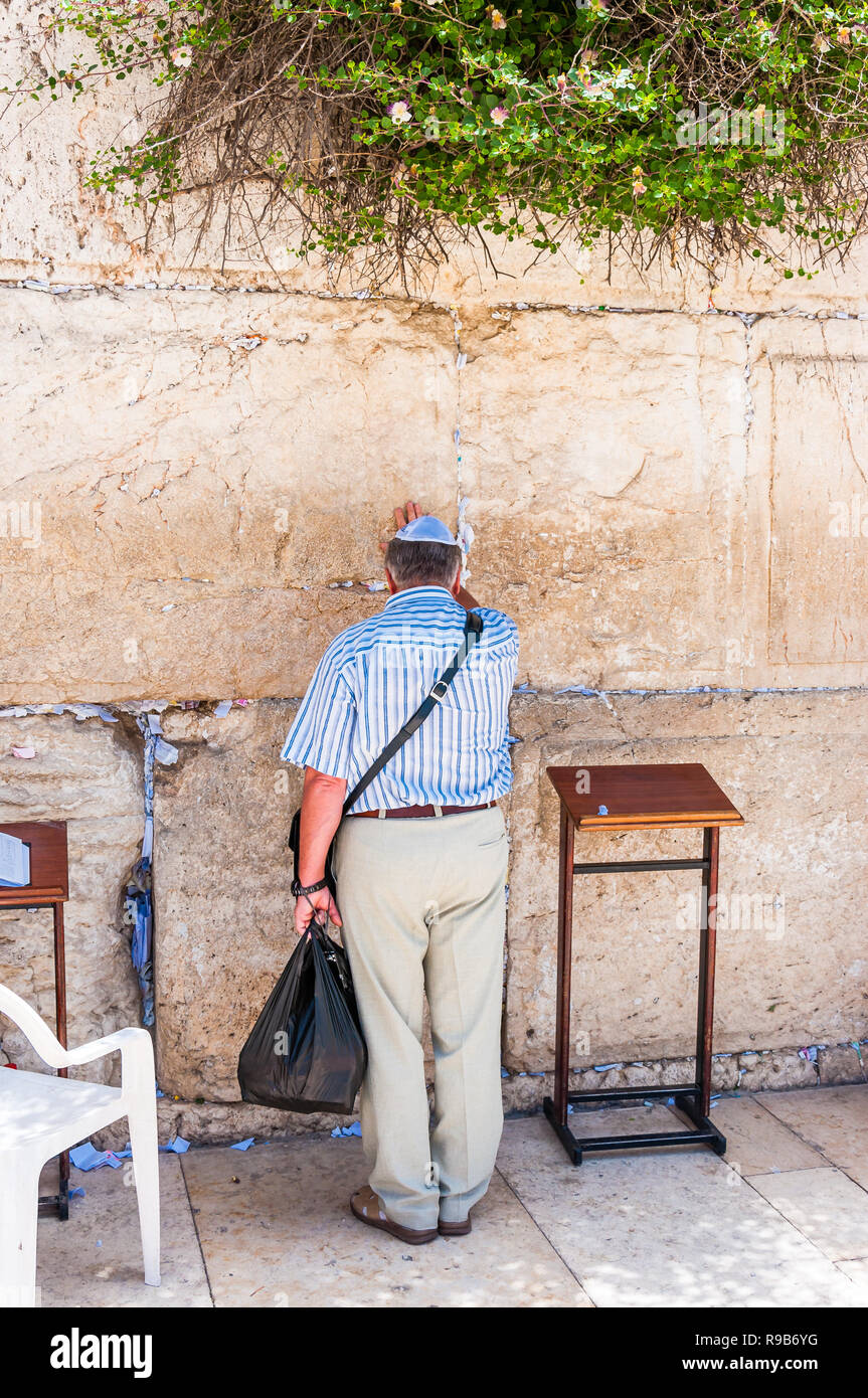 Jerusalem, Israel - 25. Mai 2012: Mann im blauen Hemd, helle Farben und schwarzen Sack berühren alten heiligen Stein der westlichen Mauer Fragen etwas her Stockfoto