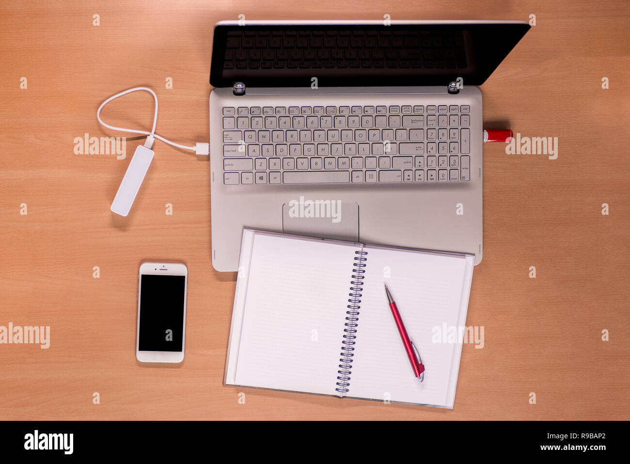 Business moderne Technologie auf dem Schreibtisch: Öffnen Sie den Laptop mit ladeleistung Bank und Memory Stick angeschlossen, Mobiltelefon und Notebook mit roter Stift Stockfoto