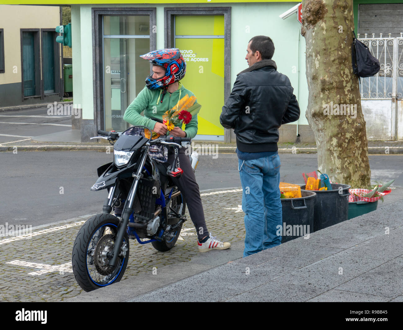 Motorrad fahrer mit Helm auf stoppt einen Blumenstrauß von einem männlichen  Street Hersteller vor 'neue Bank der Azoren" kaufen Stockfotografie - Alamy