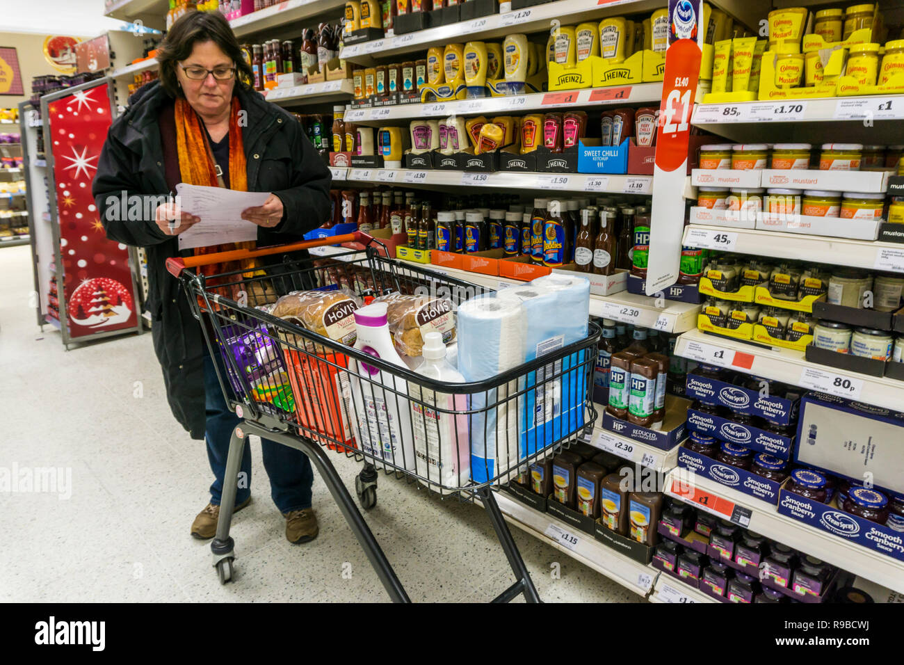 Frau die Kontrolle einer handgeschriebenen Einkaufszettel neben einem vollen Supermarkt Trolley. Belästigt, Last Minute Shopping besorgt. Stockfoto