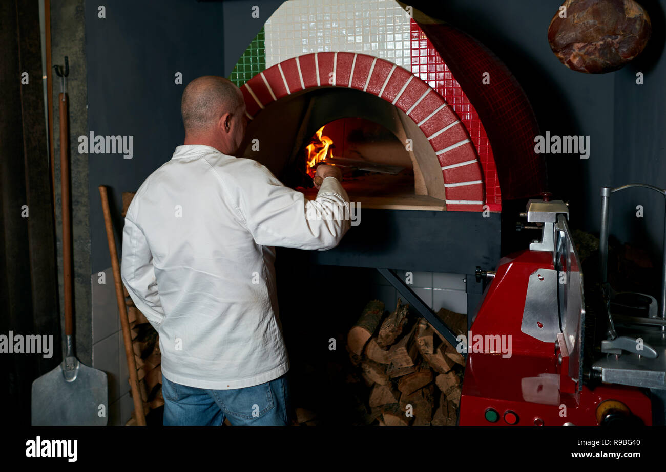 Koch zieht eine Pizza aus dem Ofen Stockfoto