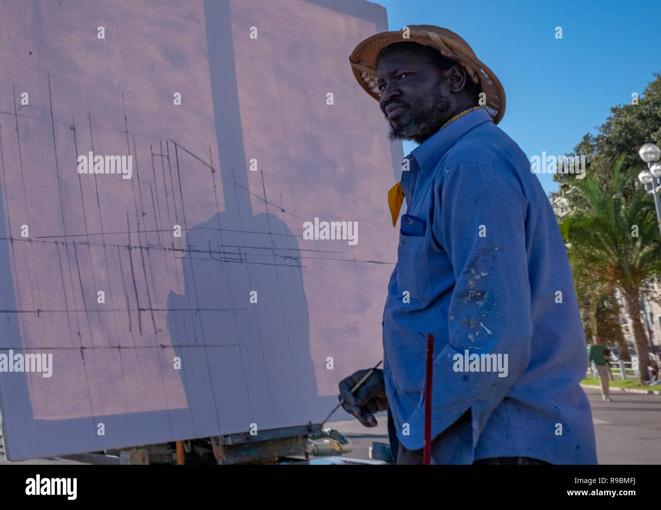 Schwarze Künstler in Safari Hut stellt seine Staffelei ein outdoor Szene mit seinem Pinsel und Leinwand zu malen. Stockfoto