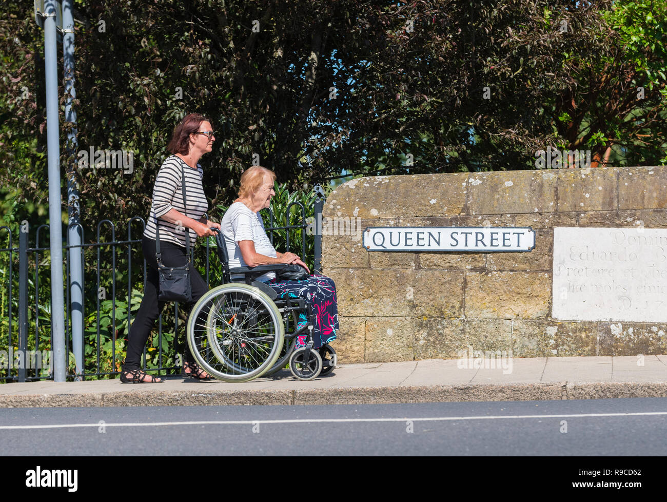 Frau drückte eine ältere Dame im Rollstuhl. Die Betreuung der älteren Menschen in Großbritannien. Stockfoto