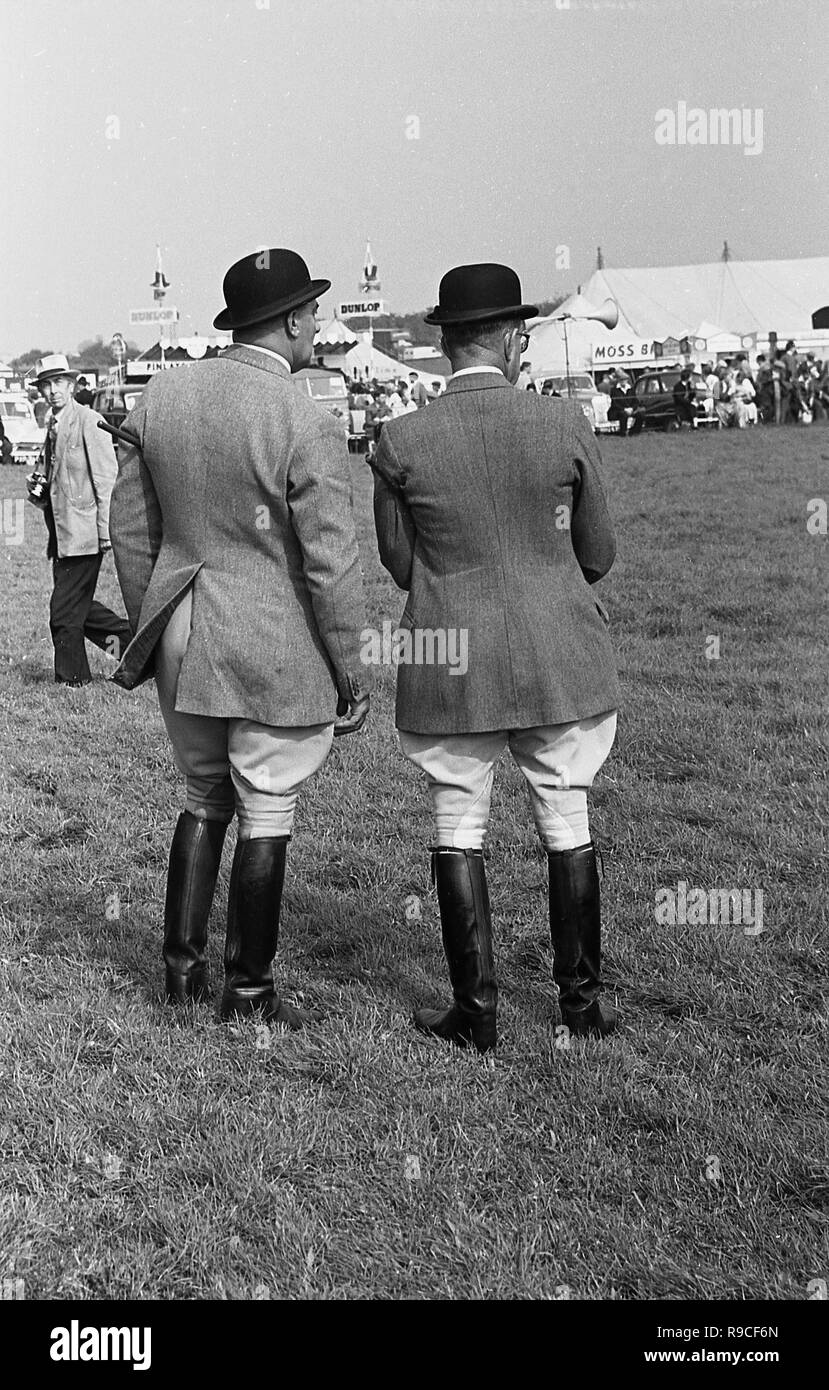 1960, an einem englischen County Fair oder Landwirtschaftliche zeigen, zwei britischen Gentleman gemeinsam in der traditionellen Land oder Riding Wear, der Bowler Hüte, Hosen, Jacken und knielange Stiefel aus Leder, England, UK. Stockfoto