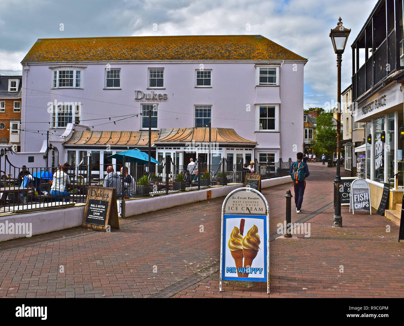 Die Menschen genießen einen entspannenden Drink in der offenen vor Dukes Hotel mit Blick auf die Esplanade und dem Meer, im traditionellen Badeort Sidmouth. Stockfoto
