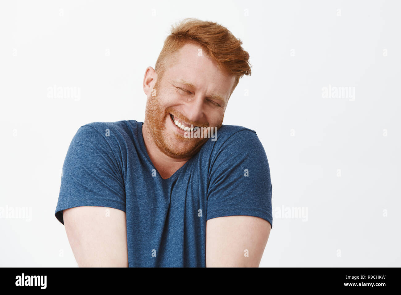 Oh, sie stoppen. Portrait von niedlichen erfreut und zufrieden glücklich und lustigen rothaarigen Mann im blauen T-Shirt, zuckte mit den Schultern und lehnte sich auf der Schulter, während breit grinsend und errötete vor Freude und Glück Stockfoto