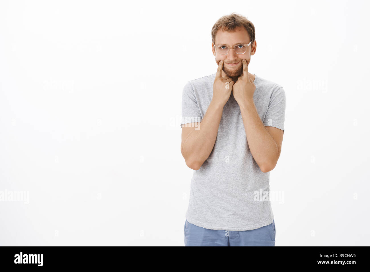 Kerl oben eingezogen vorgibt, er okay ziehen glückliches Lächeln auf dem Gesicht aber Gefühl düsterer und unglücklich stretching Grinsen mit Finger auf die Lippen Ecken gleichgültig und unvorsichtig an Kamera starrt auf weißem Hintergrund Stockfoto