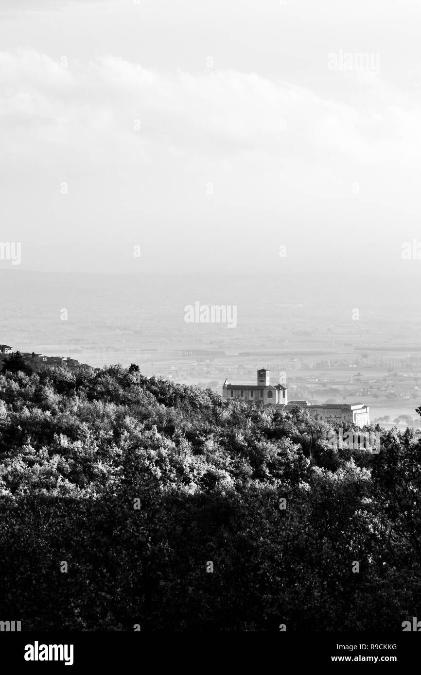 Wunderschöne Aussicht auf die Stadt Assisi (Umbrien) im Herbst von einem ungewöhnlichen Ort, hinter einem Hügel mit Bäumen Stockfoto