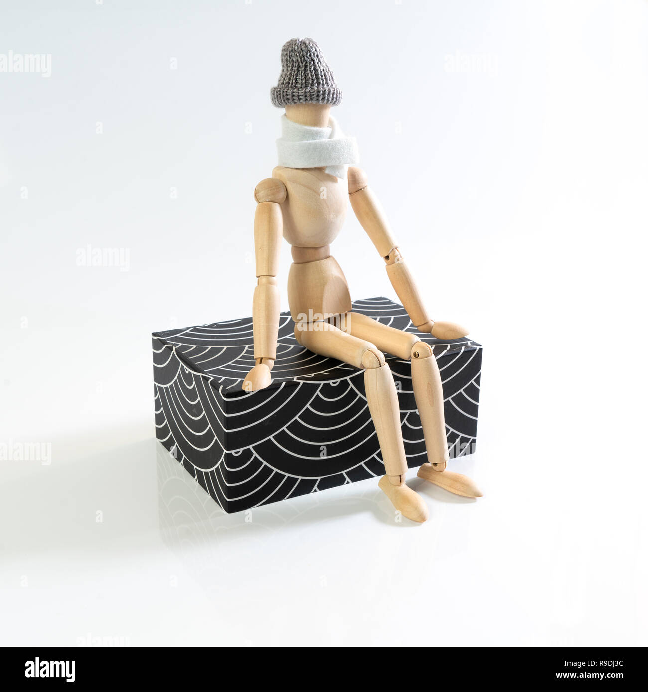 Eine hölzerne Puppe mit Schal und Mütze sitzt auf einem parallelepiped Stockfoto