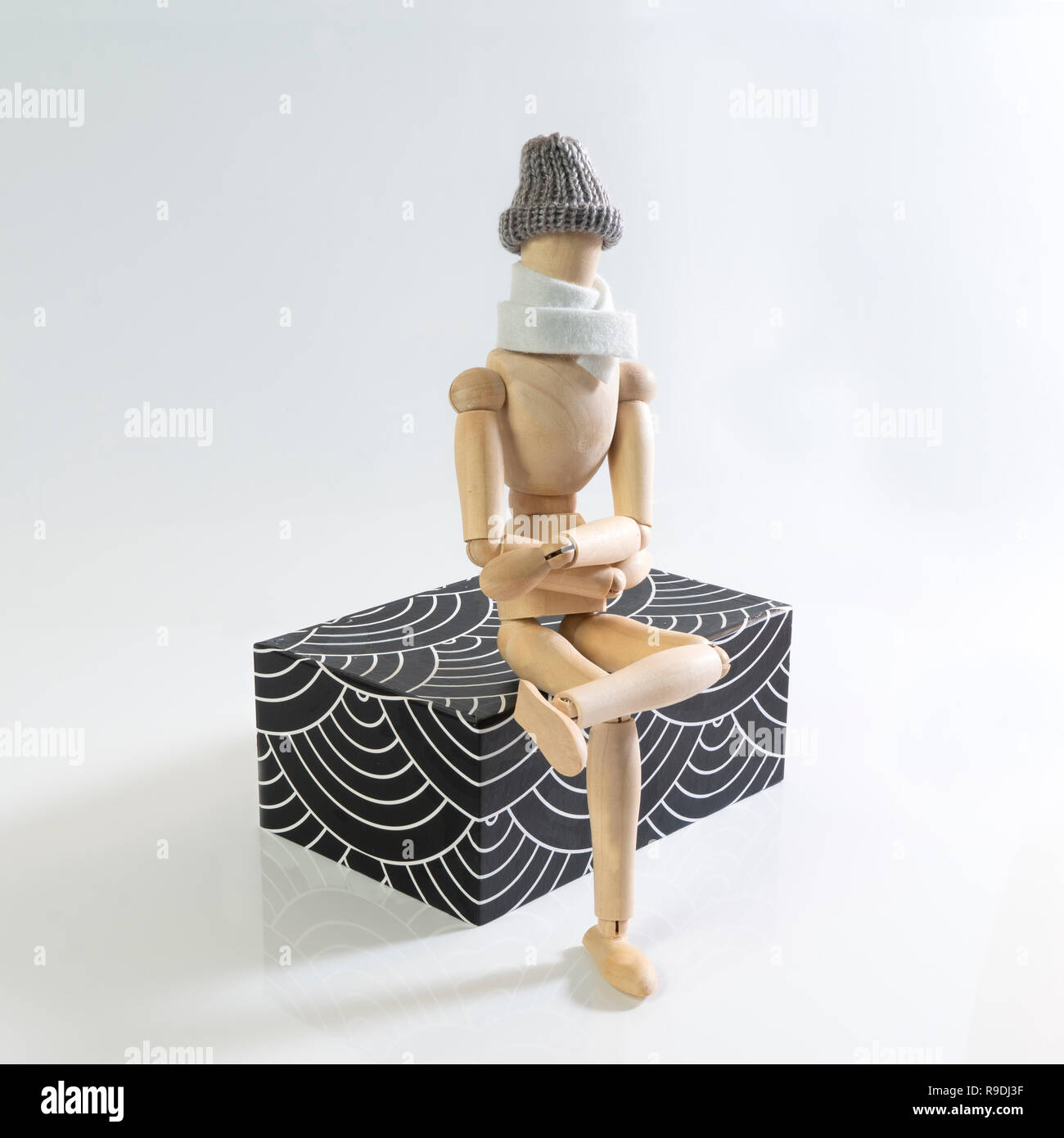Eine hölzerne Puppe mit Schal und Mütze sitzt auf einem parallelepiped Stockfoto
