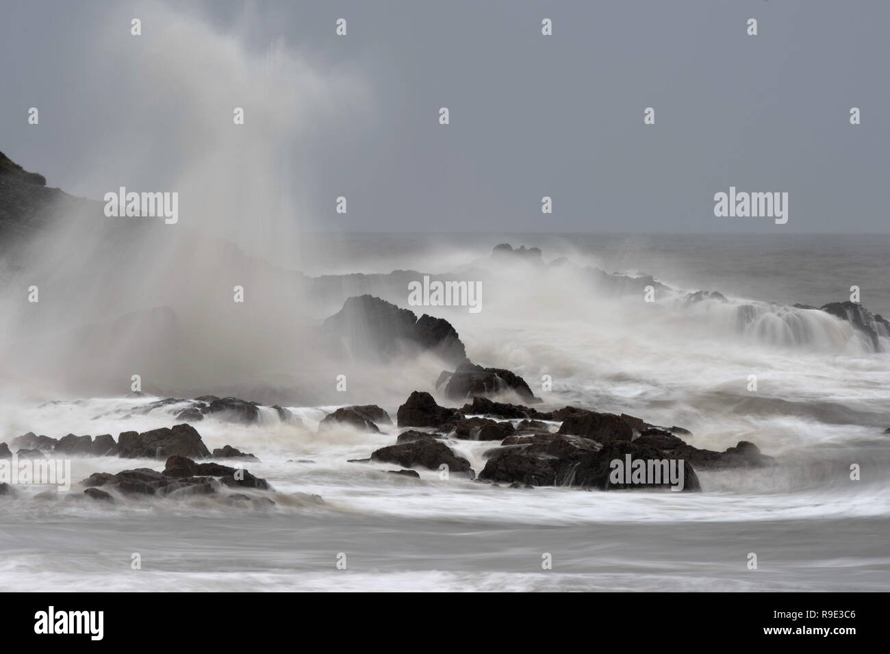 Spray von Sturmflut hängt in der Luft über der zerklüfteten Felsen wo Wellen und Schaum rush zwischen den Felsen. Stockfoto