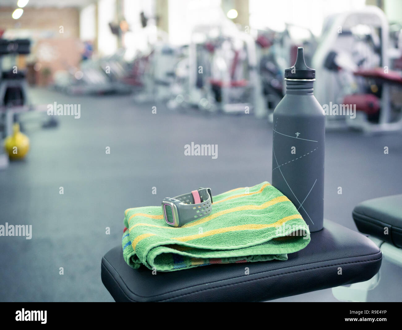 Nahaufnahme einer Wasserflasche und Sportuhr in einem Fitnessstudio Sitzbank mit Threadmills und Ausbildung Maschinen verschwommen auf Hintergrund. anaerobe oder aerobe Fitness Gy Stockfoto