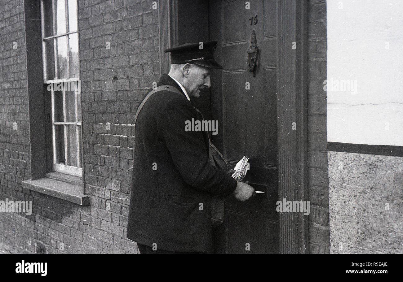 1940er Jahre, eine Royal Mail Briefträger die Post durch eine Haustür Briefkasten eines viktorianischen Reihenhaus, England, Großbritannien Stockfoto