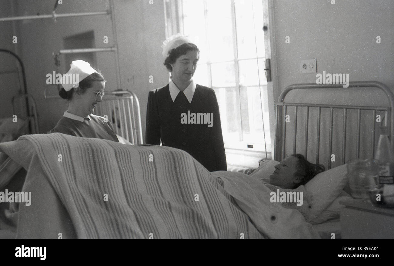 1940er Jahre, auf eine post-Krieg britische Krankenstation, eine matrone oder Schwester und eine junge Krankenschwester im Gespräch mit einer Dame Patient in einem Metall Bett lag, England, UK. Stockfoto