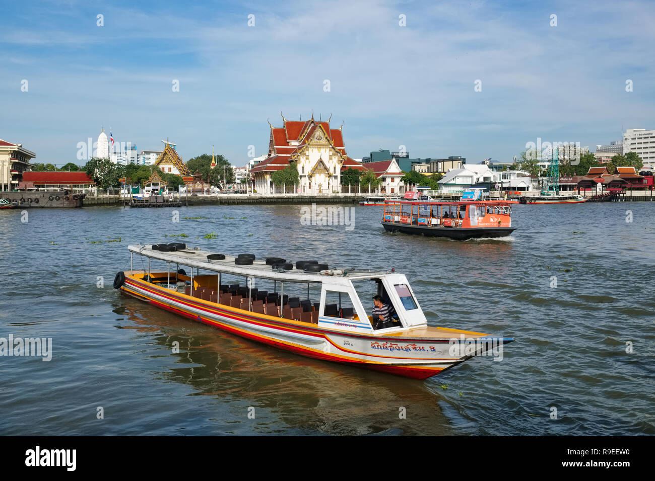 Ein touristenboot (vorne) und einem Fluss mit der Fähre (hinten) auf dem Fluss Chao Phraya, Bangkok, Thailand; im Hintergrund der Tempel Wat Rakhang Stockfoto
