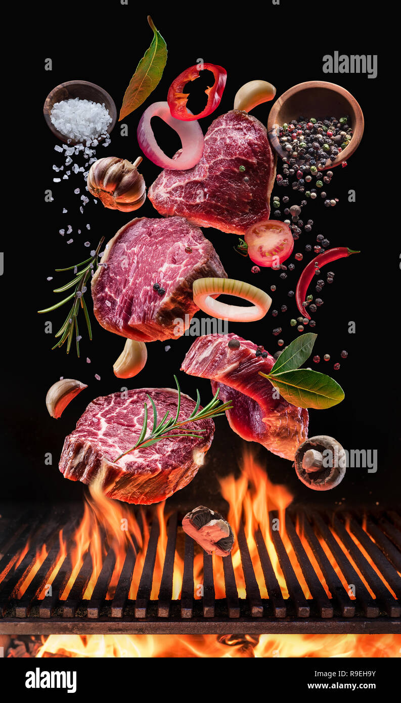 Rohes Rindfleisch Steaks mit Gemüse und Gewürze fliegen über den brennenden Grill Grill Feuer. Konzept der Flying Food. Stockfoto