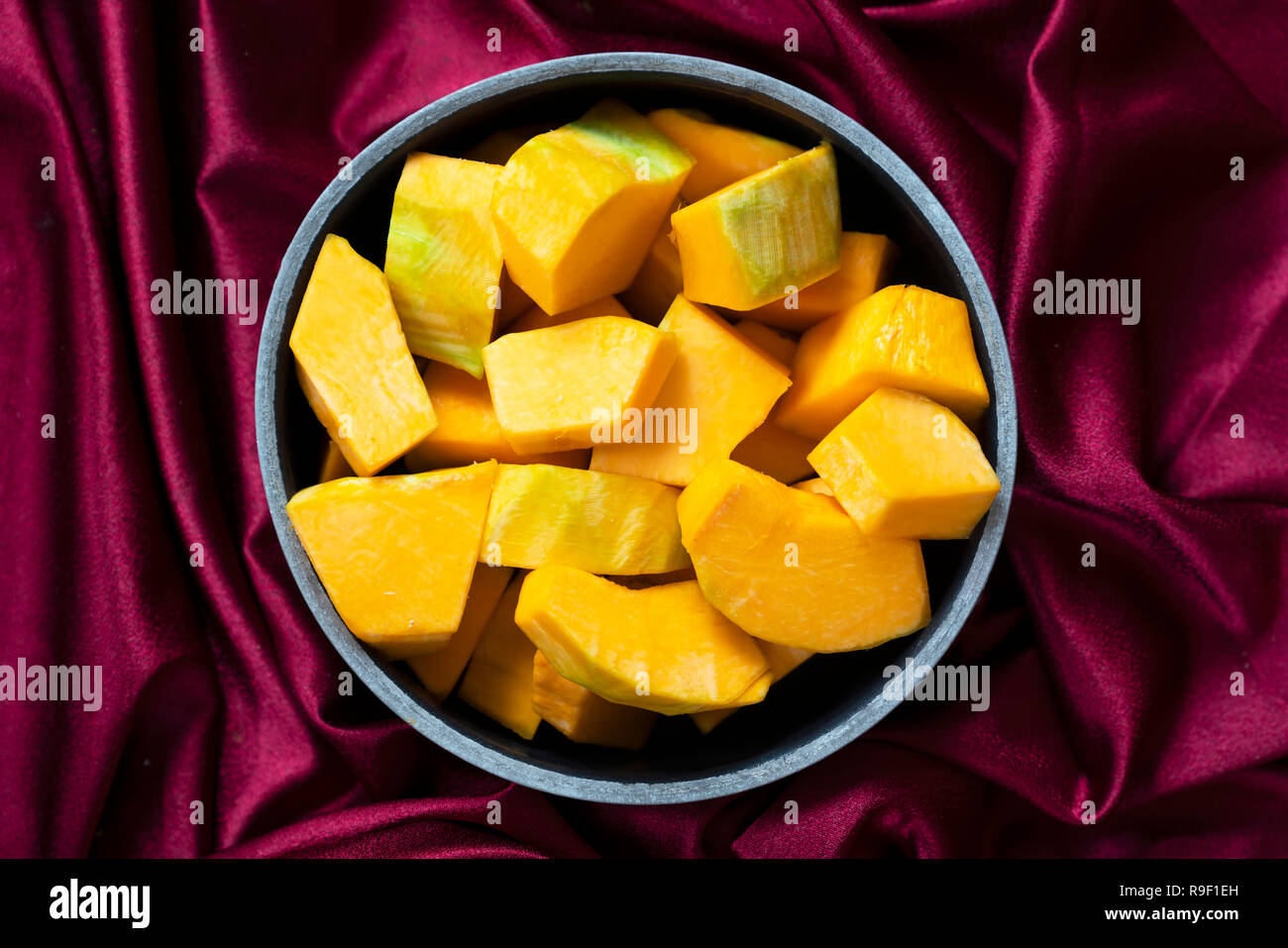 Stücke von Kürbis in einem schwarzen Schüssel mit rotem Stoff Hintergrund. Stücke von Kürbis sind bereit, traditionelle türkische Kürbis Dessert namens Kabak tat zu kochen Stockfoto