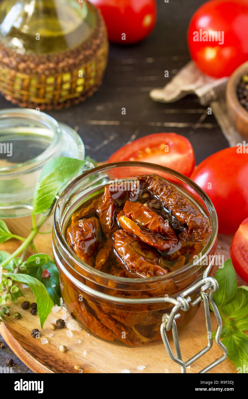 Sonnengetrocknete Tomaten mit Olivenöl in einem Glas auf schwarzen Stein oder Beton. Stockfoto