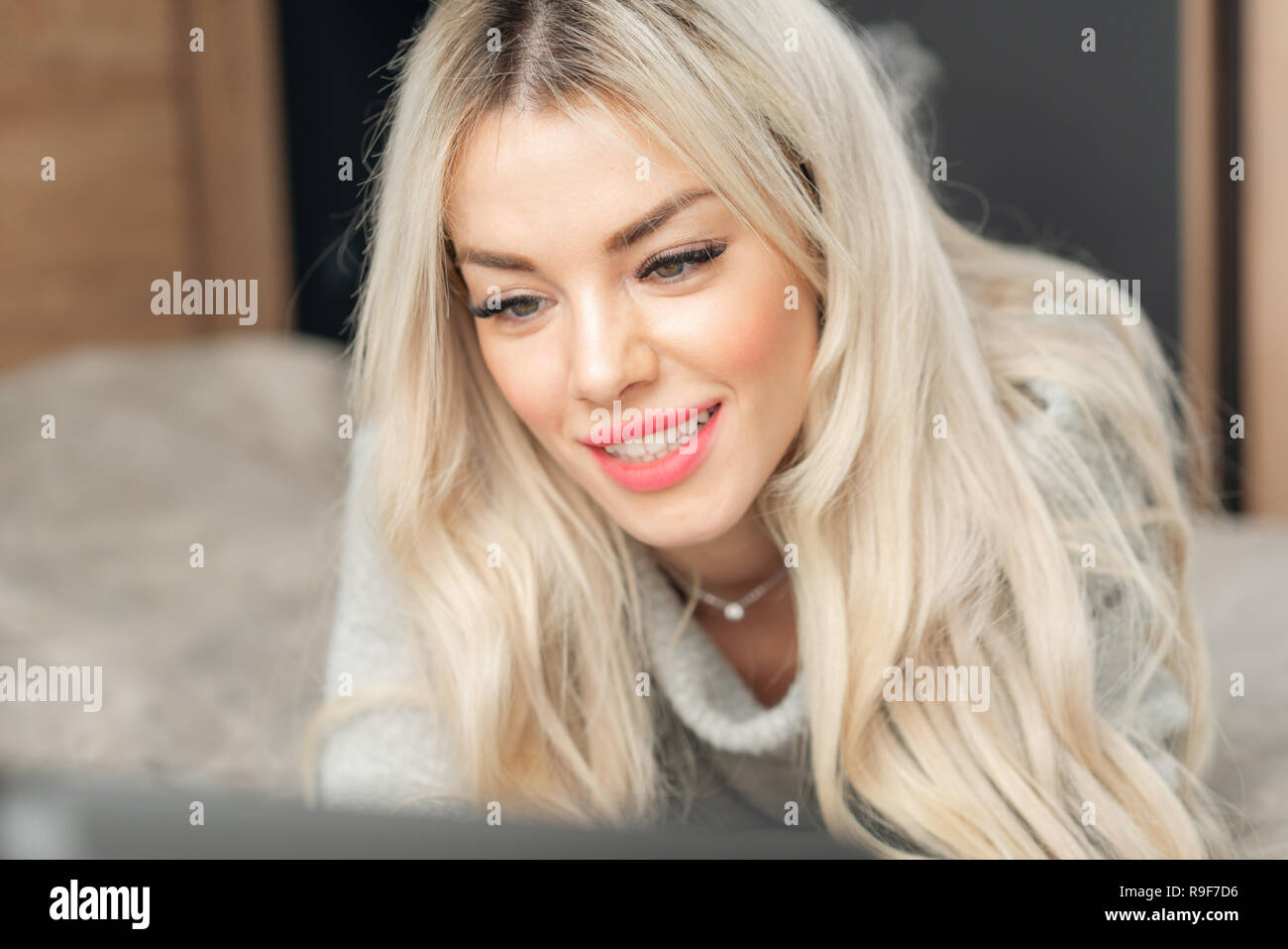 Porträt eines Mädchens hinter einem Laptop Bildschirm. Schöne blonde Frau auf dem Bett und schaut sich der Bildschirm des Laptops. Blogging, Internet surfen, chatten Stockfoto