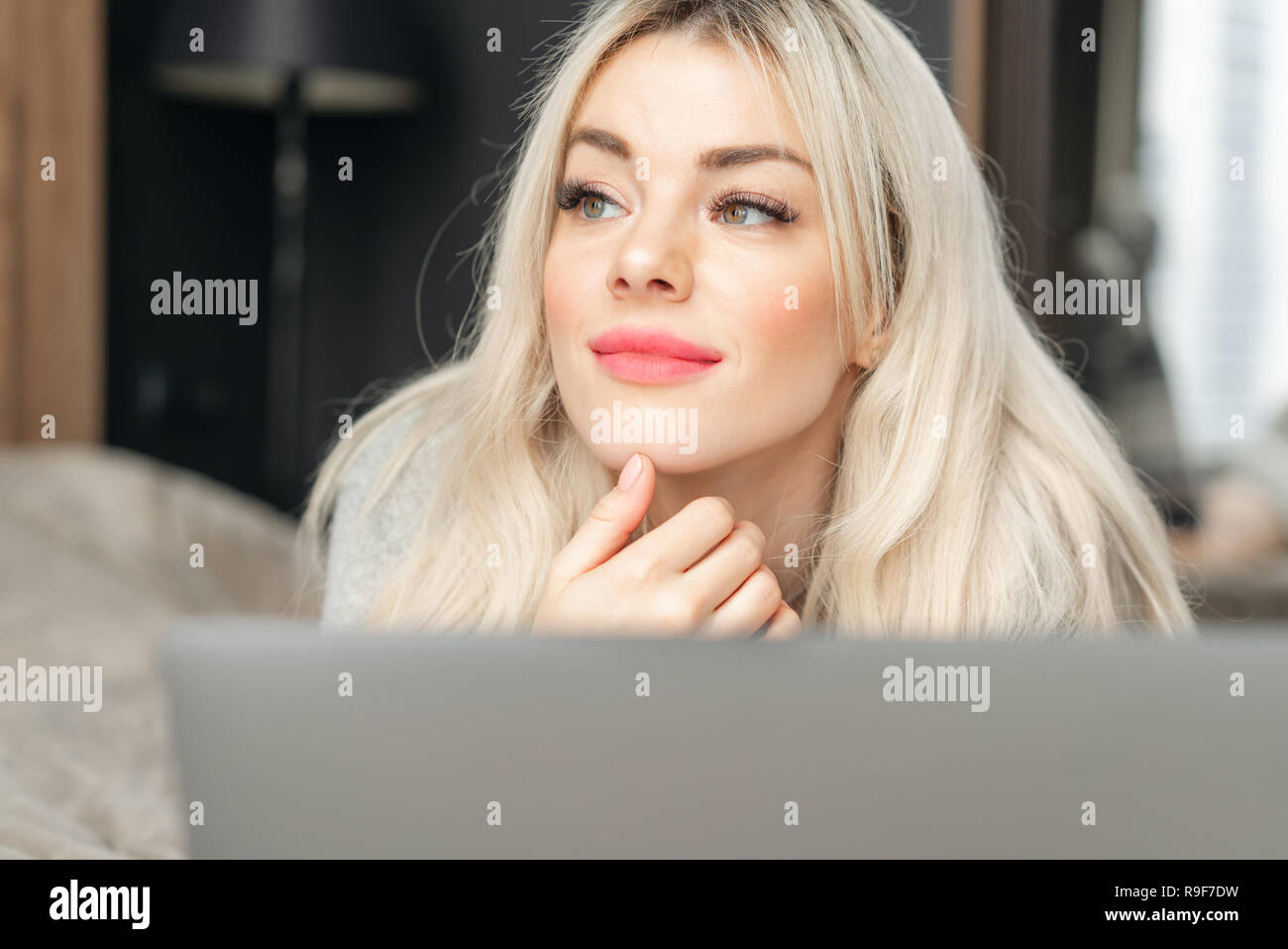 Porträt eines Mädchens hinter einem Laptop Bildschirm. Schöne blonde Frau auf dem Bett und schaut sich der Bildschirm des Laptops. Blogging, Internet surfen, chatten Stockfoto