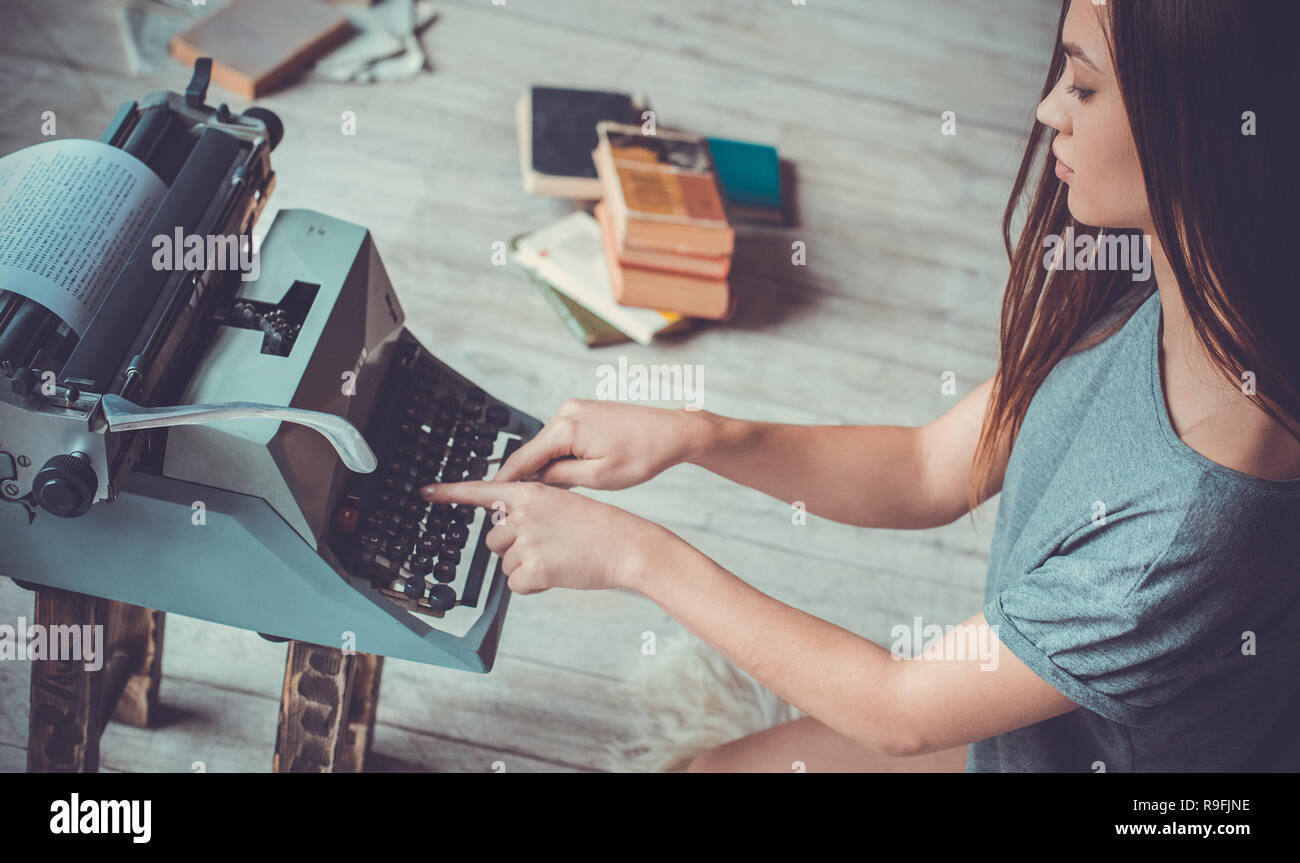 Junge weibliche Schriftsteller in der Bibliothek drinnen Arbeitsraum mit zerknittertem Papier sitzen auf dem Teppich schreiben Artikel zu Schreibmaschine suchen Durcheinander konzentriert Stockfoto