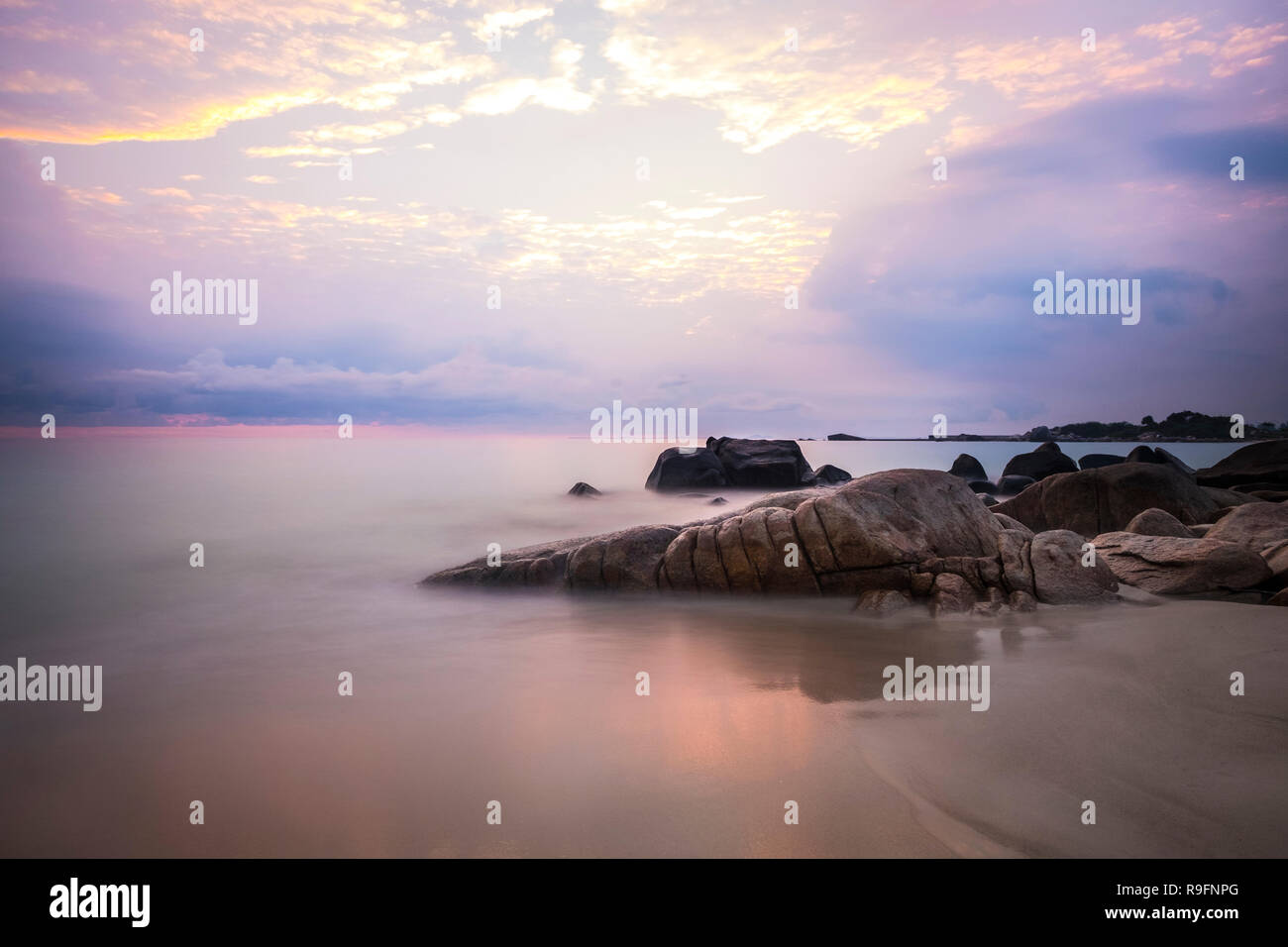 Sonnenaufgang an der Insel Bintan. Sand meer himmel wolken und Steine Stockfoto