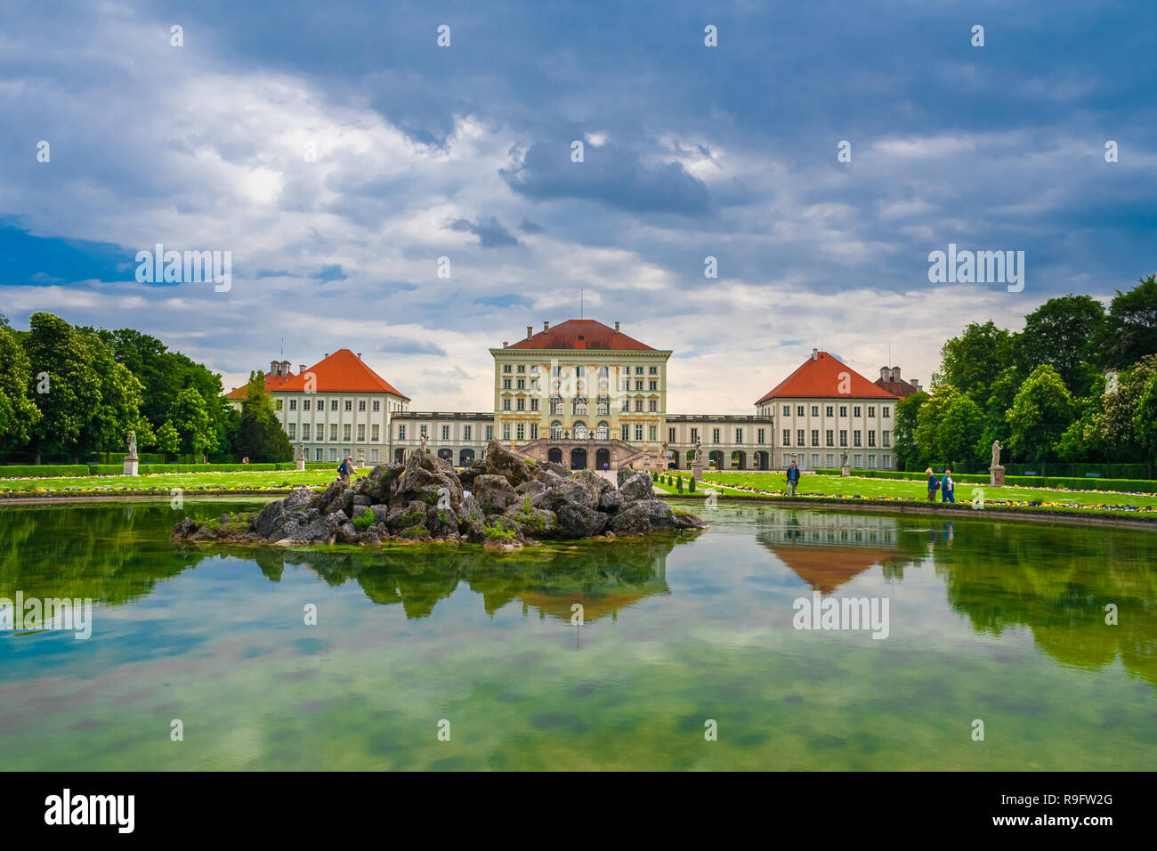 Schöne Panoramasicht auf die Fontäne im Großen Parterre mit Wasser Reflexionen und der Rückseite Blick auf das berühmte Schloss Nymphenburg in der... Stockfoto