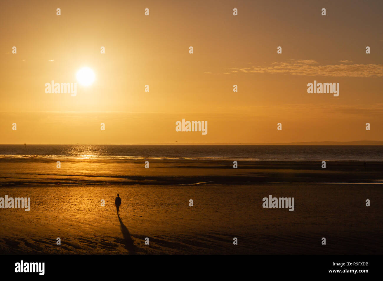 Eine einsame Person in silhouette Spaziergänge am Strand auf das Meer und die untergehende Sonne. Orange das Licht der Sonne ist in den Wellen und Strand wider. Stockfoto