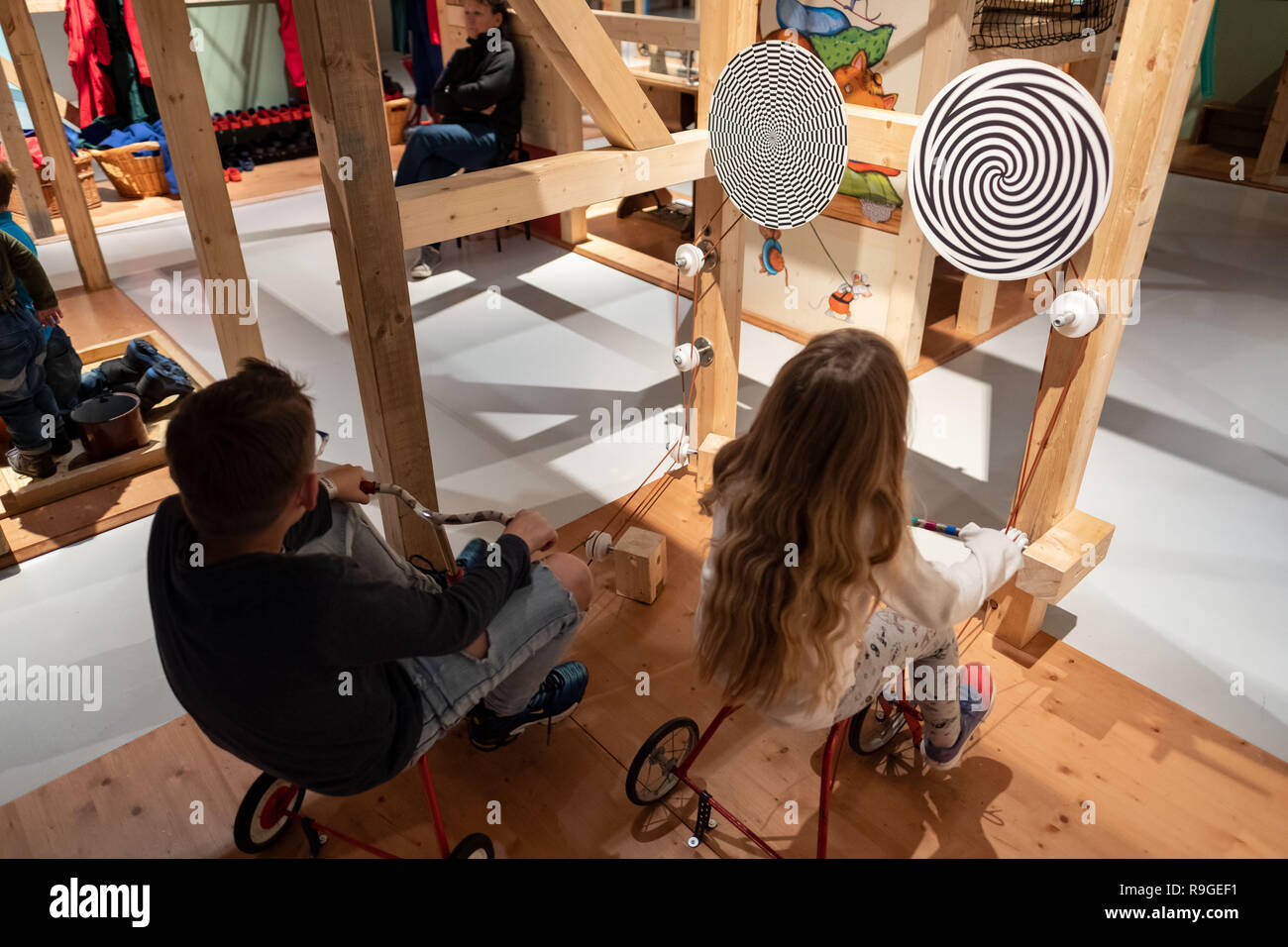 Wolfsburg, Deutschland. 23 Dez, 2018. Die besucher Noel (l) und Lia Start in der Sonderausstellung 'Tüftelmäuse' im Science Museum Phaeno mit einem Dreirar zwei rotierenden Scheiben. Mit dem 'Tüftelmäusen', die Ausstellung die Besucher eintauchen in eine Welt voller Fantasie, in der ihre erfinderischen Geist erwacht ist. In einem "Dachboden", sie erwarten zahlreiche interaktive Stationen, wo Sie ihren Einfallsreichtum beweisen können und ihre volle körperliche Engagement zeigen. Zusammen stellen sie die Maschinen in Bewegung mit Rädern, Gürtel und Zahnräder. Credit: Peter Steffen/dpa/Alamy leben Nachrichten Stockfoto